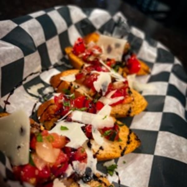 Steel House bruschetta with diced tomatoes, balsamic glaze, and shaved cheese on checkered paper.