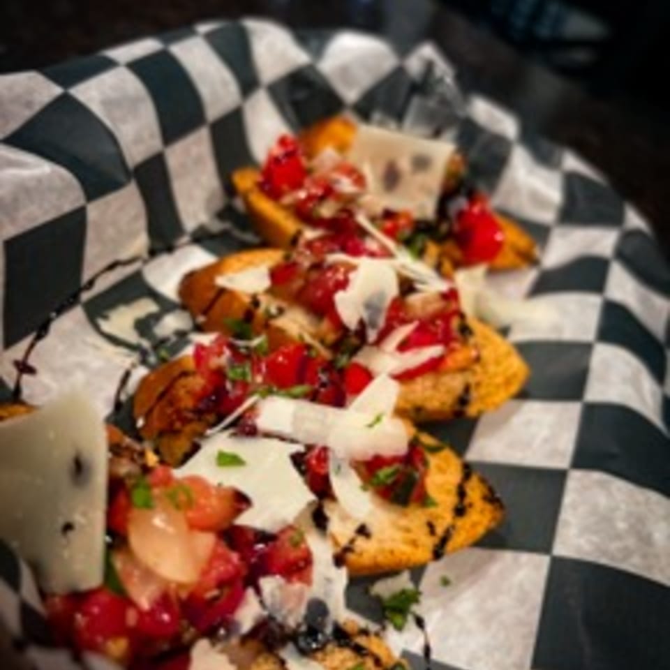 Steel House bruschetta with diced tomatoes, balsamic glaze, and shaved cheese on checkered paper.