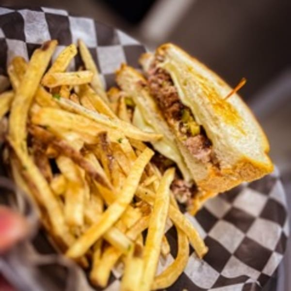 A Steel House cheesesteak sandwich with fries, served in a checkered paper-lined basket.