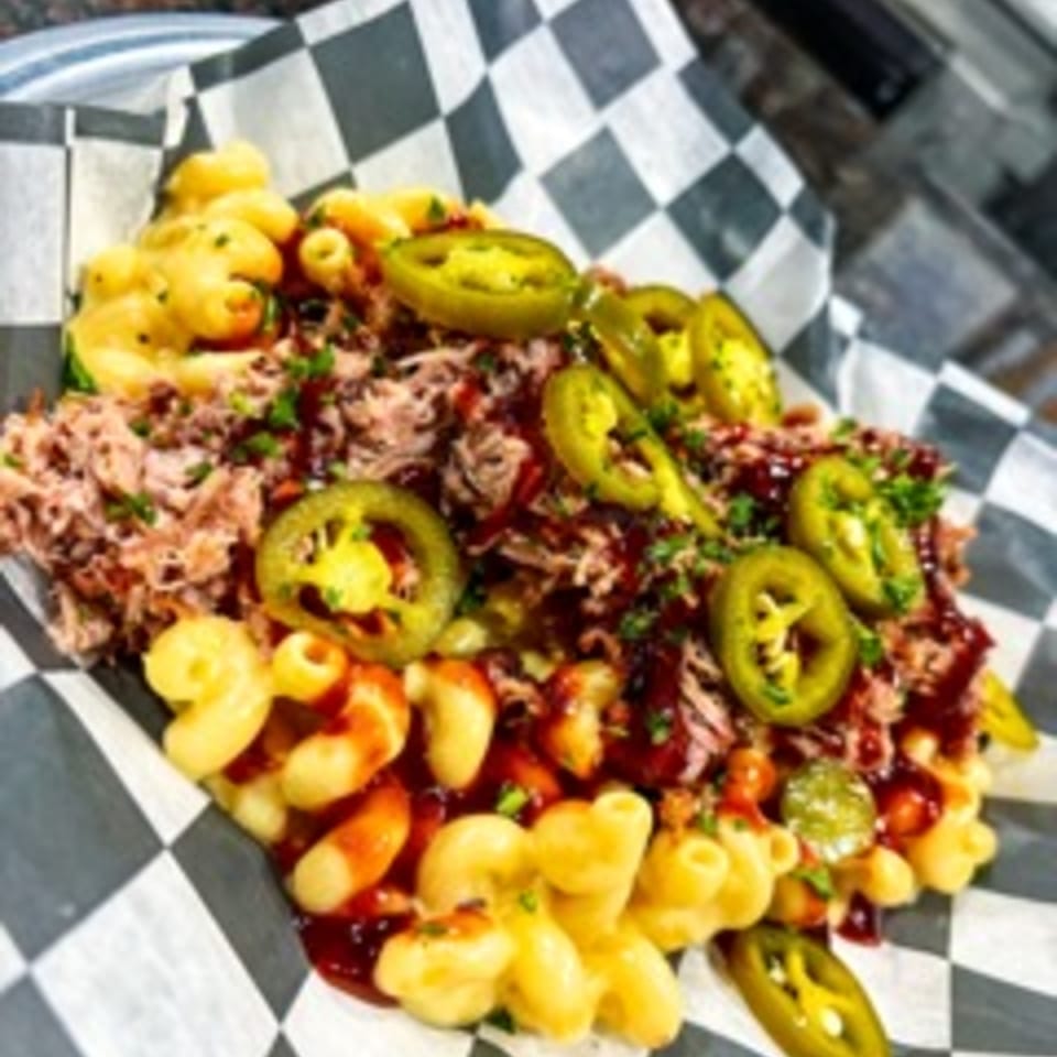 Steel House's pulled pork mac and cheese, topped with jalapeños and barbecue sauce, on checkered paper.