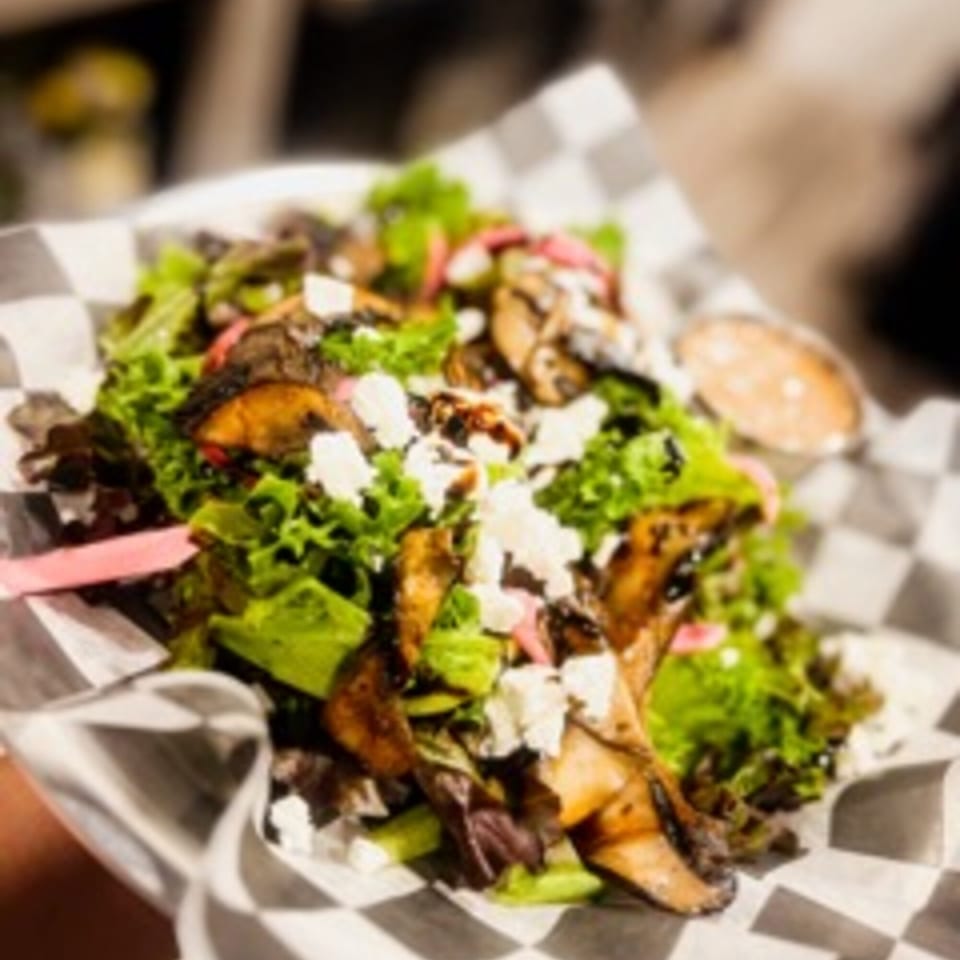 Steel House bar-&-grill's salad with mushrooms, feta, avocado, and pickled onions in a checkered paper-lined basket.
