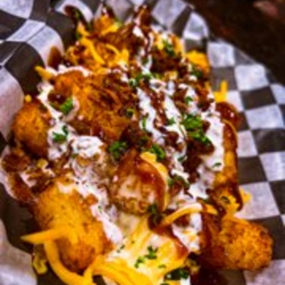Loaded tater tots with cheese, bacon, sour cream, and chives in a checkered paper-lined basket.