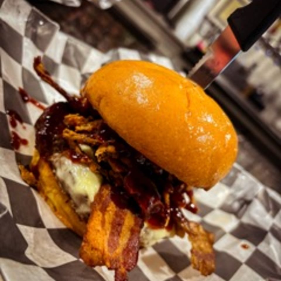 A Steel House burger with bacon, cheese, and BBQ sauce, served on checkered paper.