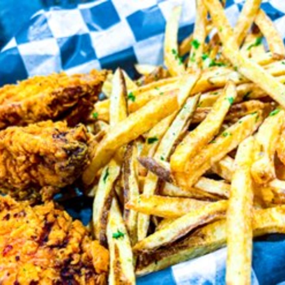 Crispy fried chicken pieces and golden french fries with parsley in a blue checkered basket.