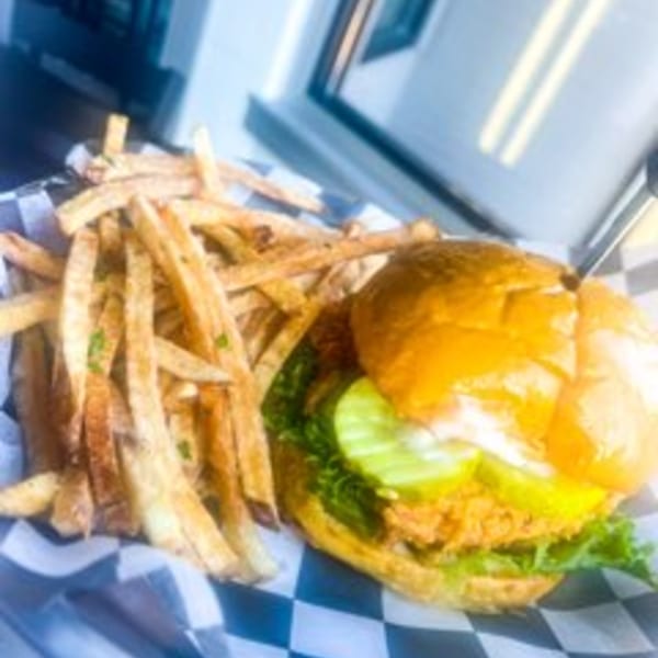 Steel House fried chicken sandwich with pickles, lettuce, and fries on a checkered paper.